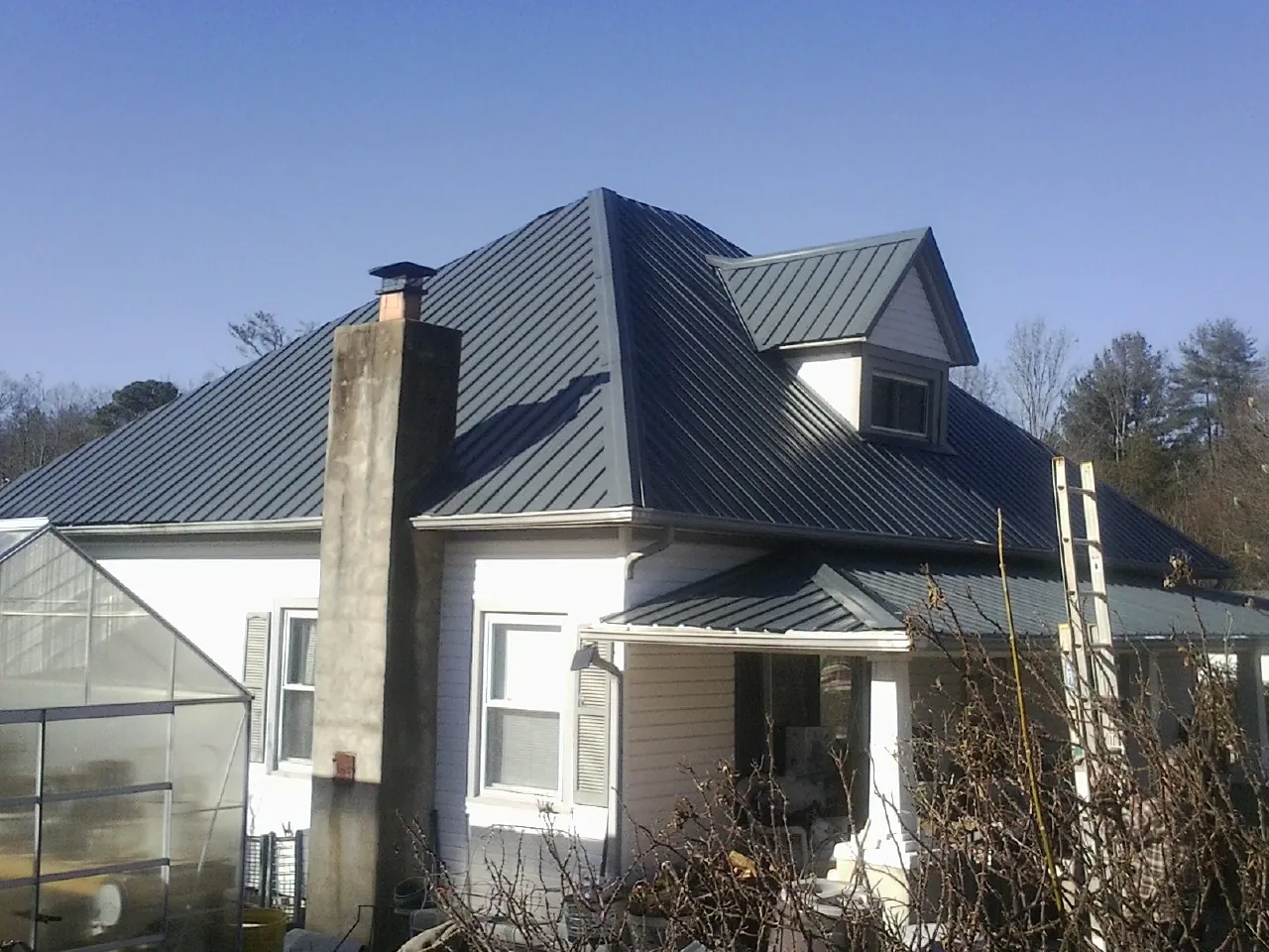Dark blue standing seam metal roof on a white farmhouse with dormer — Slate & Tile Roof Repair by Roofing Brothers in North Prairie
