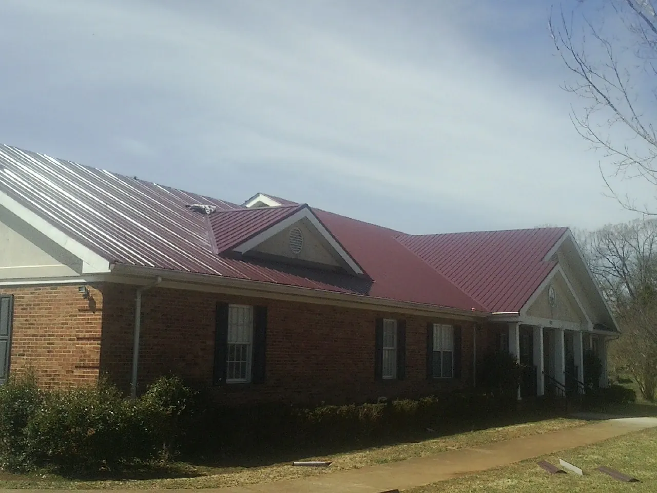 Red metal roof with gabled entries on a long brick building, from a Hail Damage Roof Repair job in North Prairie