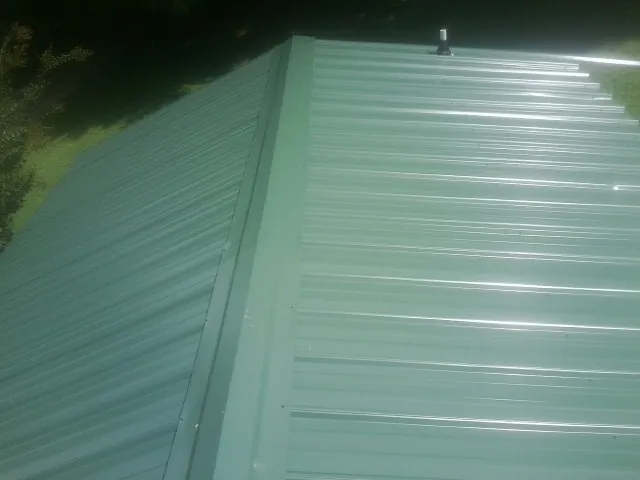 New green metal panels meeting at the ridge of a roof — Flat Roof Repair work by our crew in North Prairie
