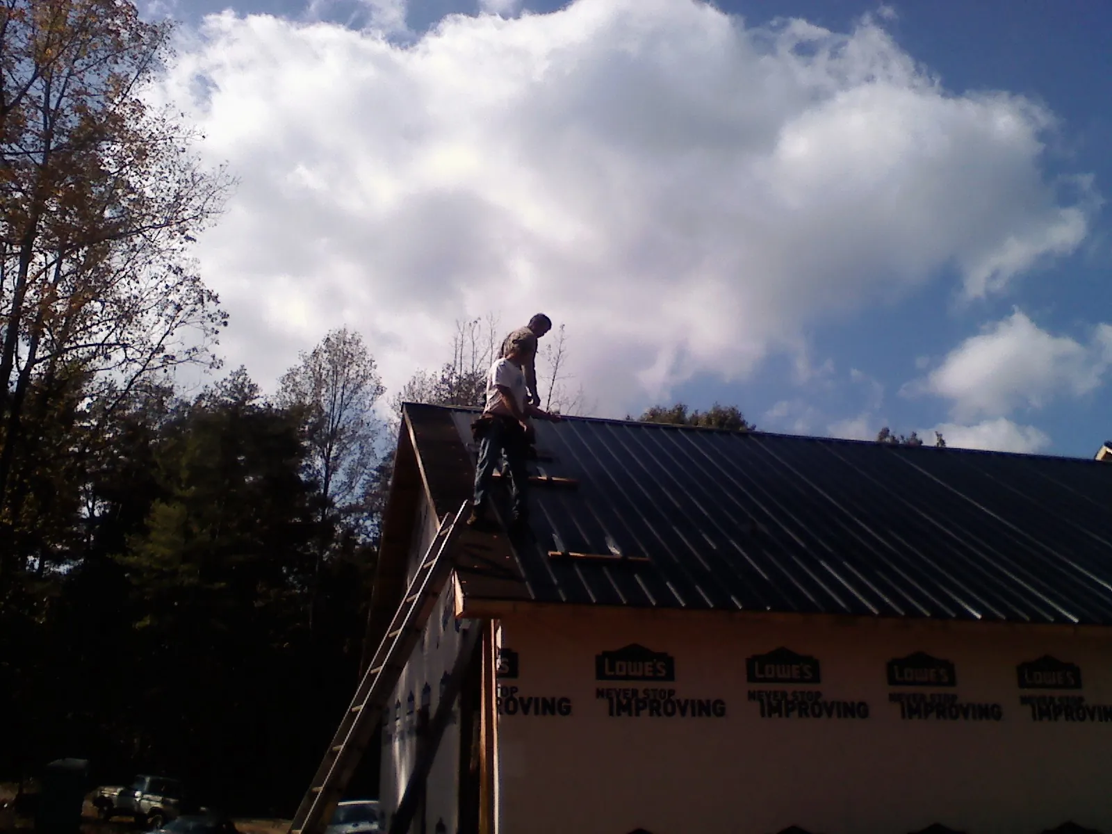 Roofer fastening dark metal panels high against a cloudy sky, from a Roof Inspection job in North Prairie