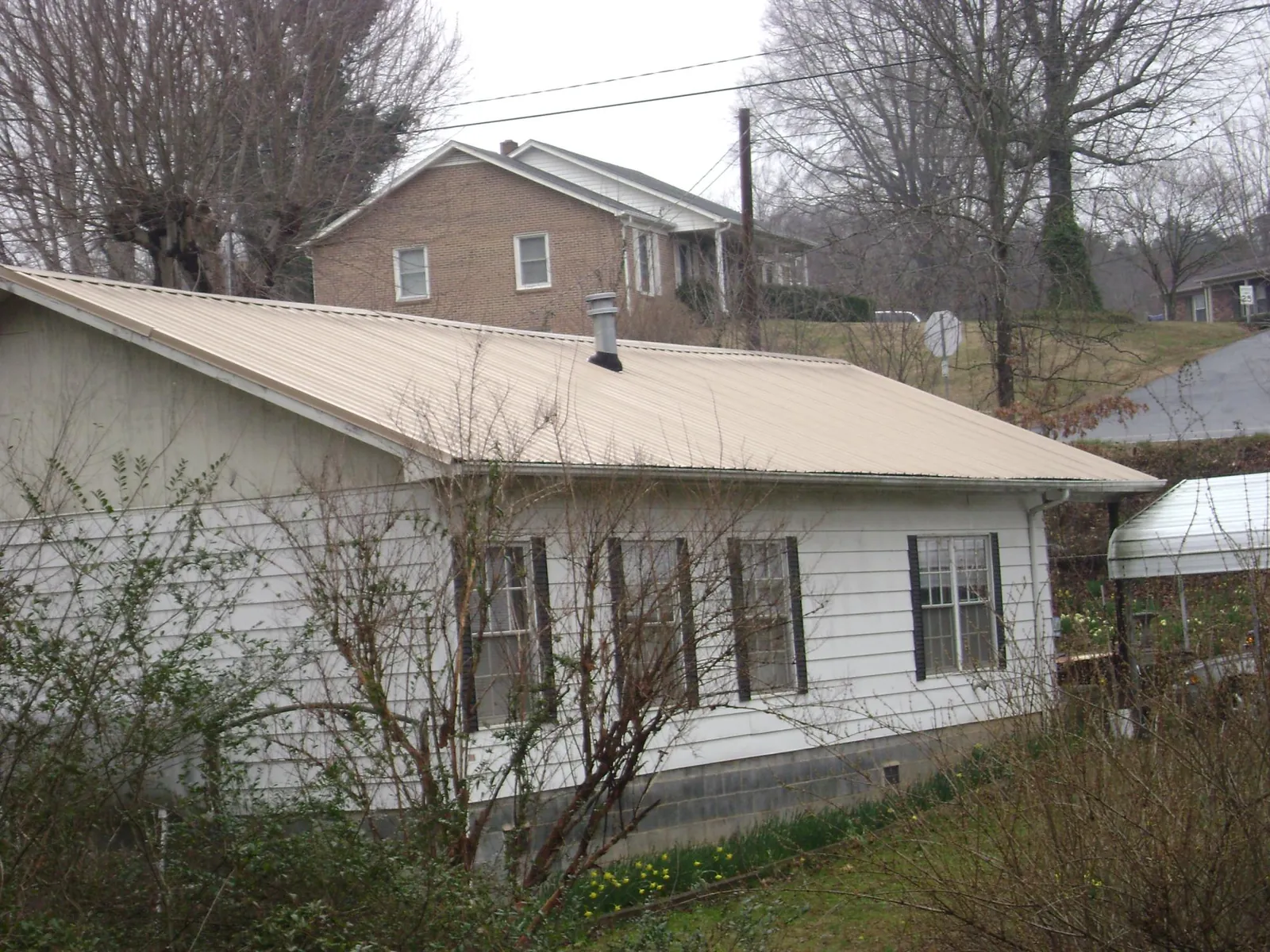Tan metal roof on a white sided house set into a hillside — Commercial Roofing by Roofing Brothers in North Prairie